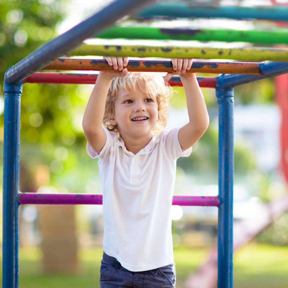 A child smiles while playing on monkey bars
