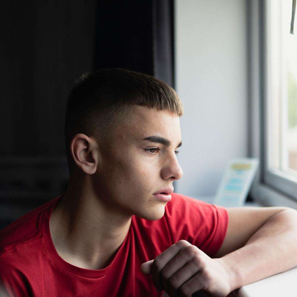 A young person unhappily looks through a window