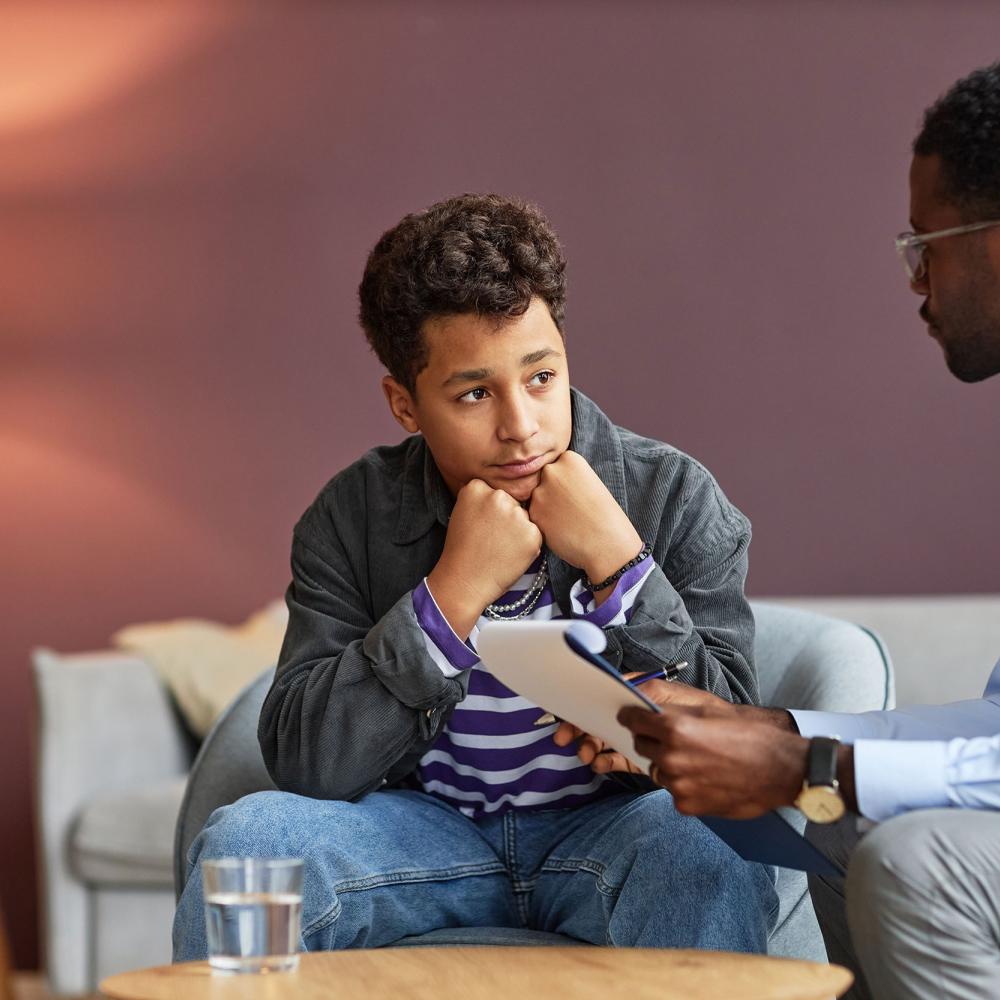 A boy sits and listens to a man holding a clipboard