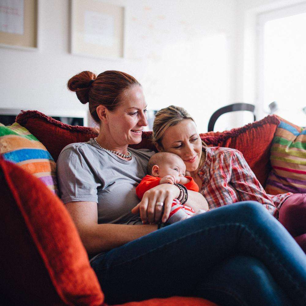 Female couple hold baby and relax on sofa