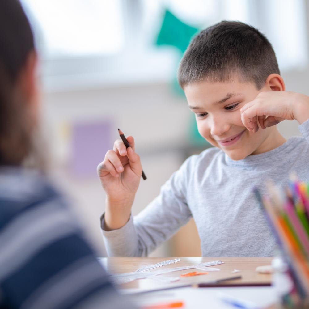 A young person smiles while holding a pencil