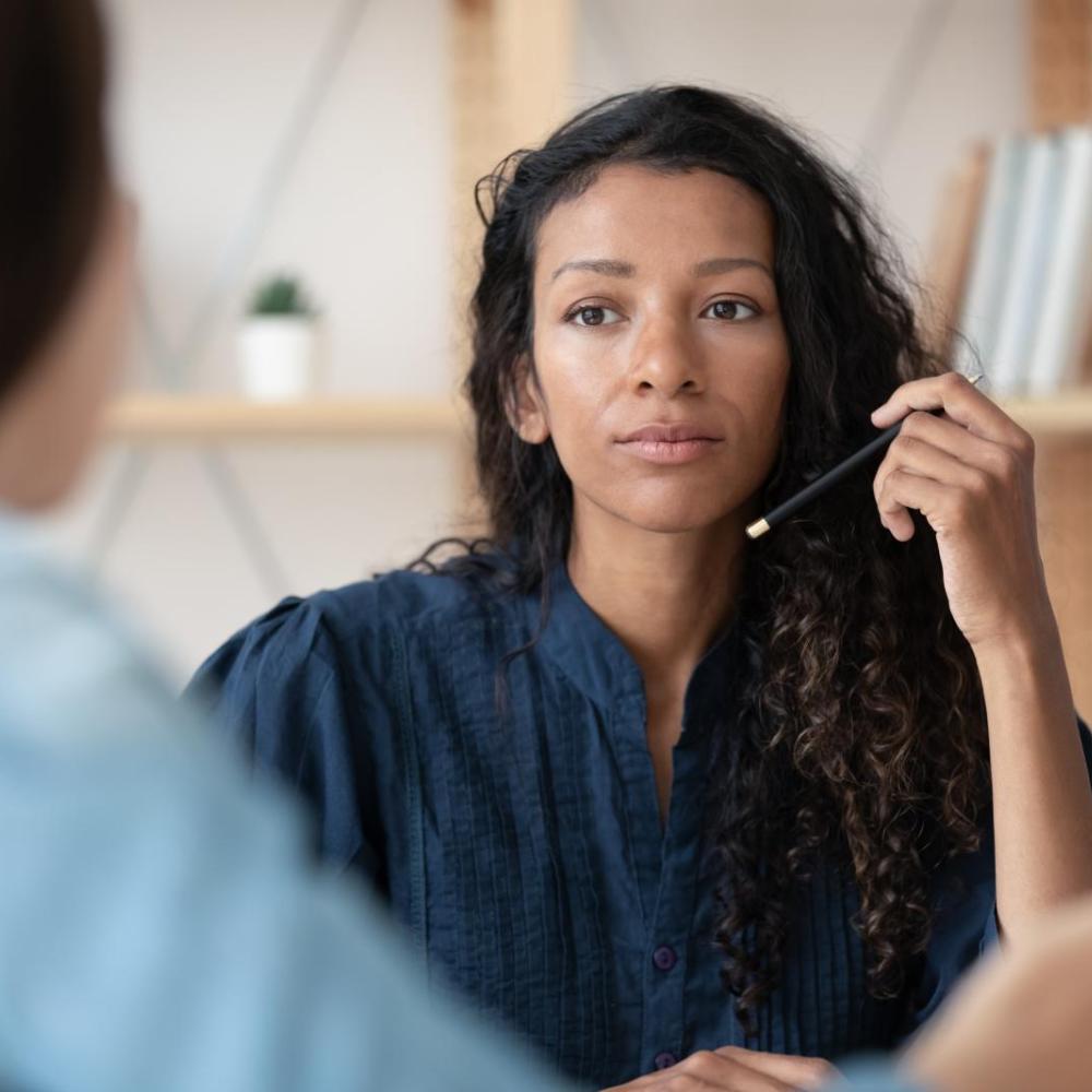 A newly qualified social worker talks with a colleague and holds a pen