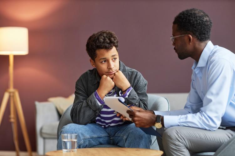 A boy sits and listens to a man holding a clipboard