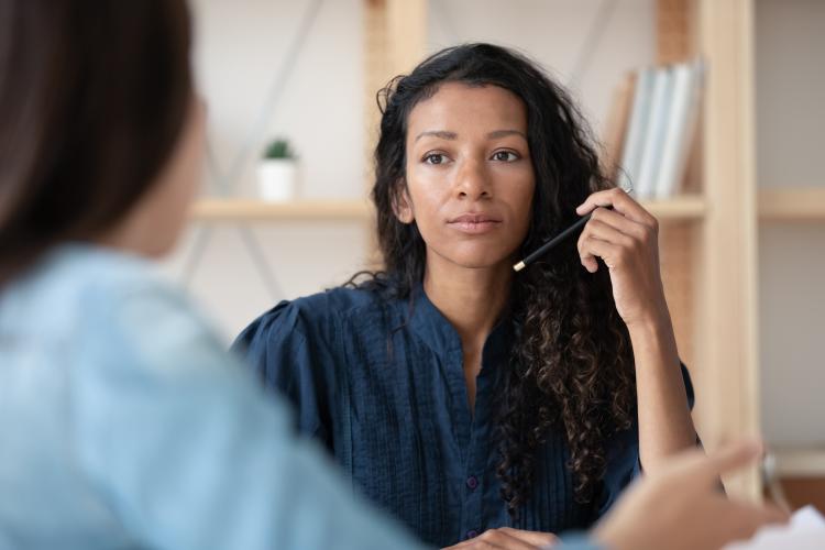 A woman talks with a colleague and holds a pen