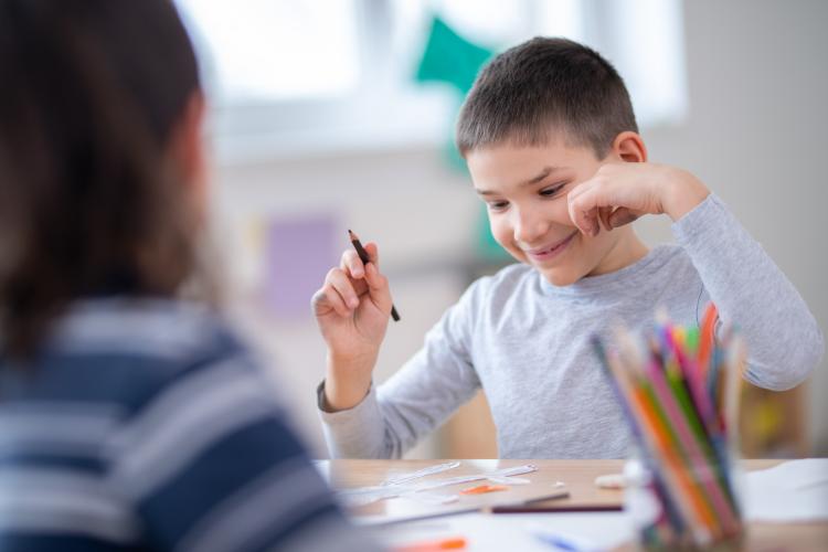 A young person smiles while holding a pencil
