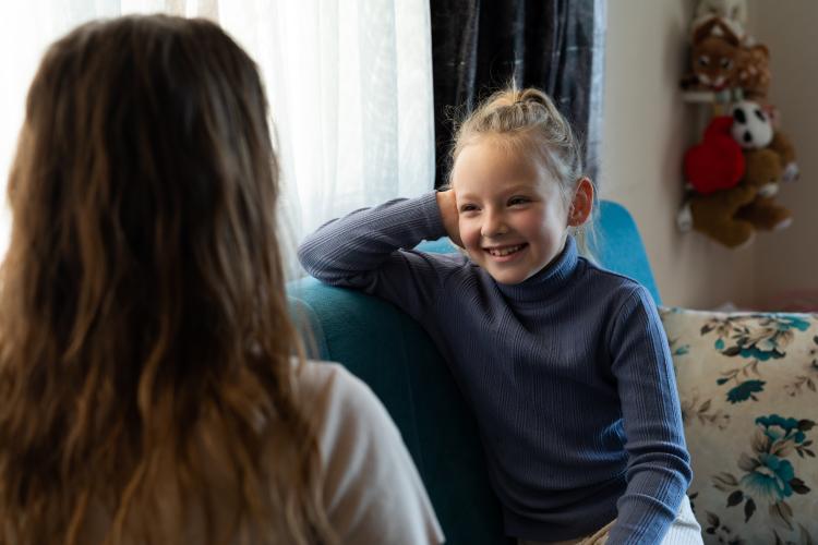 A young girl sits and smiles while talking to a social worker